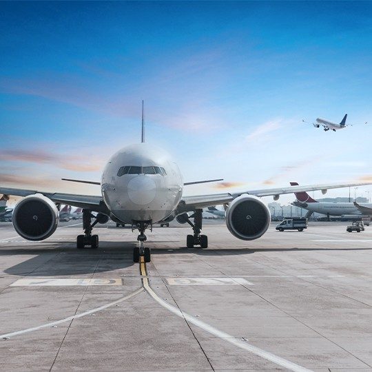 Front-view of a commercial airplane on the runway with a plane taking off in the background